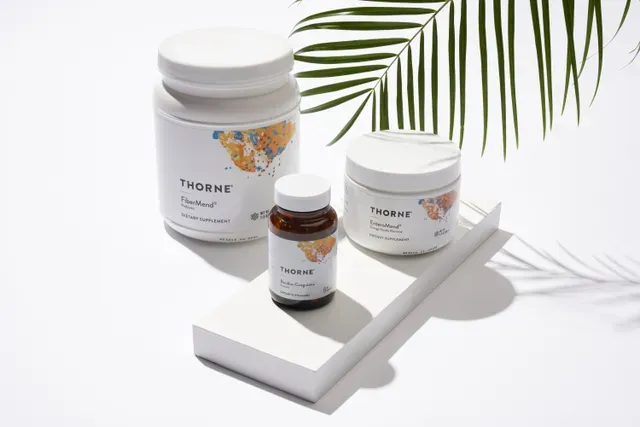 Thorne Supplements Displayed in Natural Light – pro institute Three Thorne supplement containers on a white platform with palm leaf shadow, promoting wellness and nutritional support – pro institute