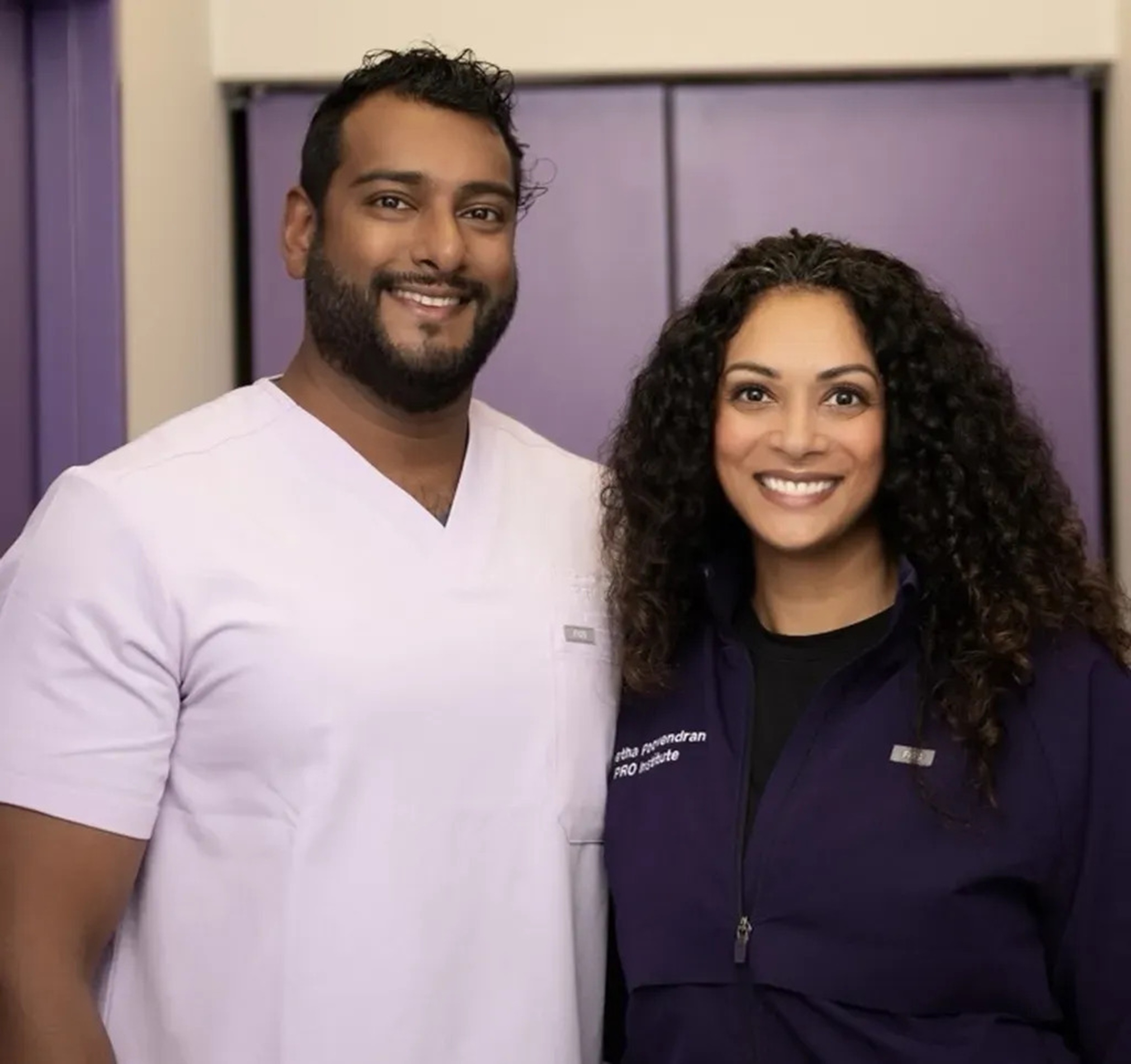 Smiling male and female healthcare providers wearing branded uniforms, standing side by side in a professional clinical setting – PRO Institute